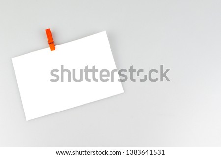Blank white horizontal poster paper attached with red and yellow clips hung on white blackground.