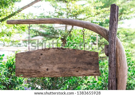 Grunge wooden blank sign board is hanging on the old curved wooden pole with the rusty chains in the public park