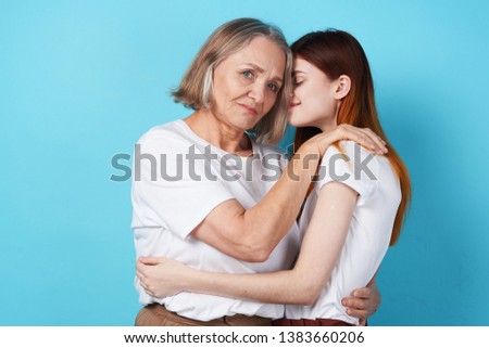 red-haired daughter and elderly mother hugging on a blue background                    