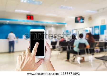Man use mobile phone, blur image of inside the bank as background. 
Financial transactions through the application can help you without having to wait on the bank's chair.