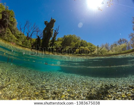 photo of half water and half sky in the blue eye waters in south albania. on the photo u can see the base of the river the sand and also the long tree and forest in the background