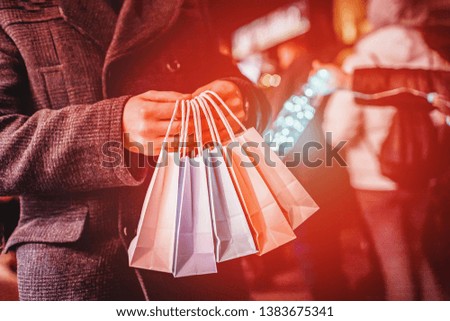 Man holding colorful shopping bags on the dark background. Sun glare effect, orange toned