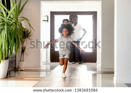 Excited African American small girl run into new home relocating with young parents, happy family moving to own house, little daughter have fun jumping in hallway. Ownership concept Royalty-Free Stock Photo #1383681086