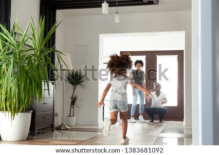 Happy little African American girl run to dad excited to meet him after work, funny small child rush to black young father return home after business trip, daddy wait to hug child in hallway Royalty-Free Stock Photo #1383681092
