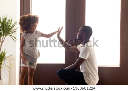 Young African American dad give high five to small cute daughter in hallway, black father and little kid make deal talking at home, parent negotiate with child having agreement. Friendship concept