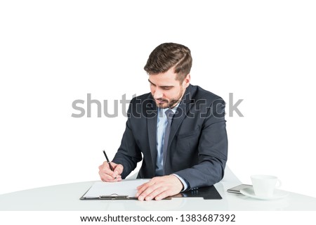 Serious young man in suit signing document at office table. Isolated portrait of young caucasian businessman. Concept of legal work and management.