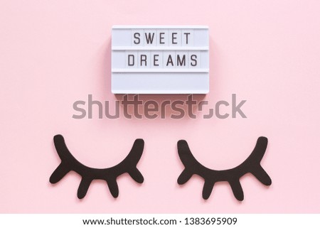 Lightbox text Sweet dreams and decorative wooden black eyelashes, closed eyes on pink paper background. Concept Good night Greeting card Top view Creative flat lay.