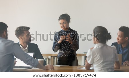 Indian female coach stand holding meeting with diverse work team discussing sharing ideas in conference room, multiethnic people or colleague brainstorm talking cooperating at office briefing Royalty-Free Stock Photo #1383719474