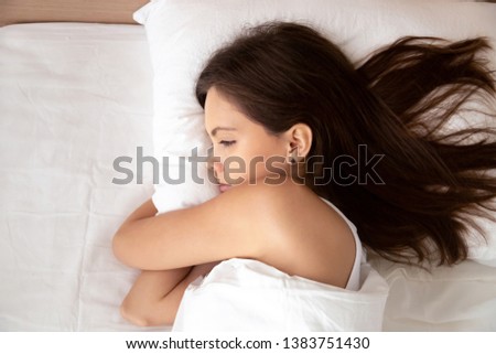 Top view of calm young woman lying in comfortable bed relax on fluffy white pillow covered with blanket, peaceful girl rest awake under warm duvet in bedroom thinking of something. Relaxation concept