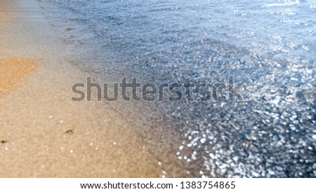 Abstract closeup out of focus photo of sea waves flowing on sandy beach at bright sunny day