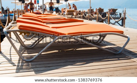 Blurred photo of people relaxing on sunbeds on the wooden pier at sea. Summer holidays on beach