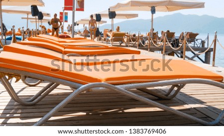Closeup photo of straight rows of sun beds on wooden pier at bright sunny day