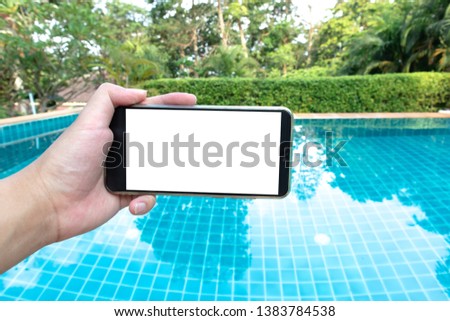 Hand holding smart phone on swimming pool background.Holiday concept.