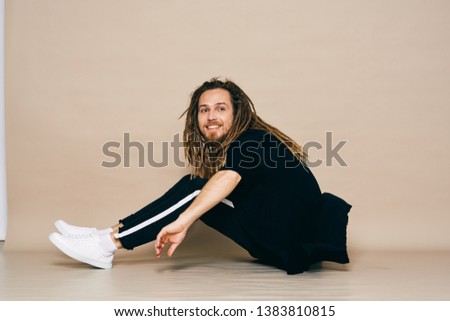A man in sports pants and a black T-shirt sits on the floor of the dreadlocks on his head                               