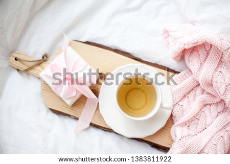 White mug with tea, gift box with ribbon on the bed. Breakfast in bed. Cozy. Pink plaid. Cotton. Spring.