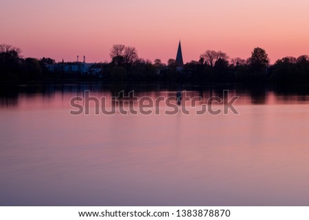 Red and pink sunset over peaceful lake with silhouette of the city of Eutin with churchtower, Schleswig-Holstein