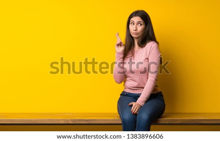 Young woman sitting on table with fingers crossing and wishing the best