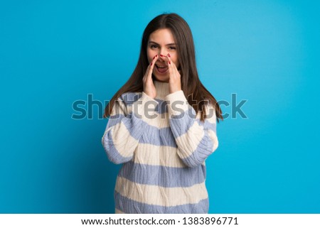 Young woman over blue wall shouting and announcing something