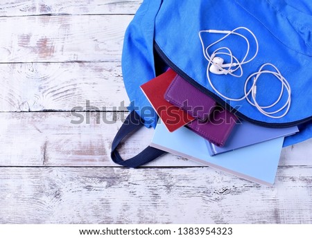 Blue backpack with books, passport, smartphone, tablet and headphones against the white background. Travel bag