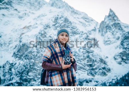 Beautiful girl makes a photo on an old vintage camera. In the mountains in winter, adventure and travel