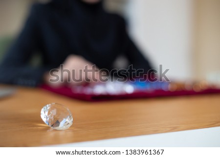 Selective focus at large jewelry on table, blurred young muslim woman is screening in background