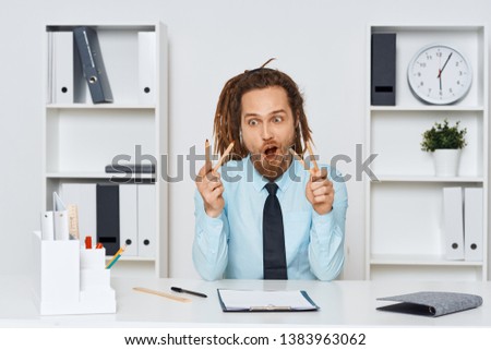 A man with dreadlocks sitting at a desk blue shirt tie office work