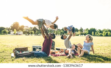 Young multiracial families having fun playing with kids at pic nic barbecue party - Multicultural joy and love concept with mixed race people together with children at park - Warm contrasted filter
