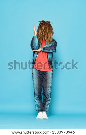man in fashionable clothes dreadlocks on his head dancing fun blue background