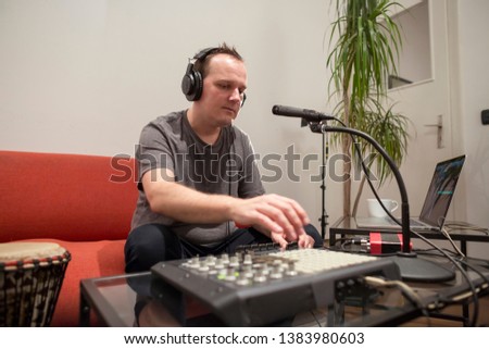 Professional musician recording midi keyboard in digital studio at home. He is surrounded with instruments and midi controller. Music production concept.