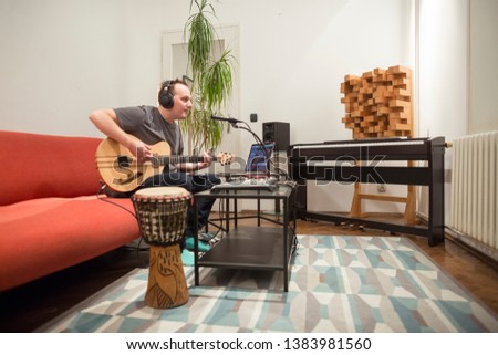 Professional musician recording electric guitar in digital studio at home. He is surrounded with instruments and midi controller. Music production concept.