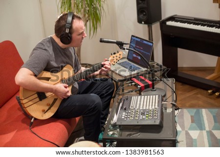 Professional musician recording electric guitar in digital studio at home. He is surrounded with instruments and midi controller. Music production concept.