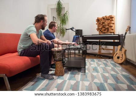 Two professional musician recording and playing instruments in digital studio at home. They are surrounded with instruments and midi controller. Music production concept.