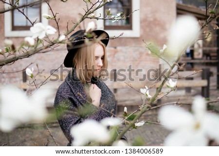 young woman with long hair in a gray long coat with a hat at sunset among flowering trees
