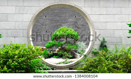 Chinese wall architecture with the circle door and brick foot path in the green garden where has full of tradition Chinese trees Royalty-Free Stock Photo #1384008104
