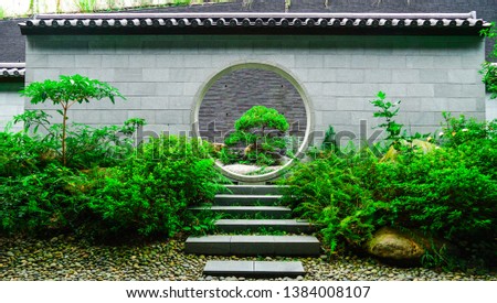 Chinese wall architecture with the circle door and brick foot path in the green garden where has full of tradition Chinese trees Royalty-Free Stock Photo #1384008107