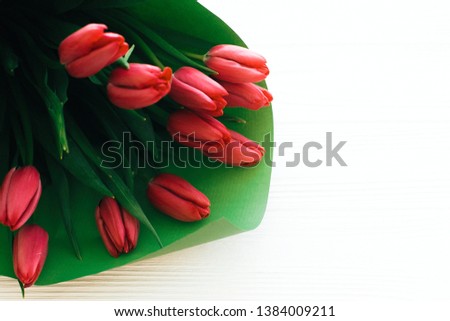 Beautiful pink tulips bouquet in green paper on white wooden background, top view. Happy mothers day. Red tulips close up on white wood with space for text. Greeting card template.