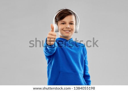 childhood, audio equipment and technology concept - portrait of smiling boy in headphones and blue hoodie listening to music over grey background