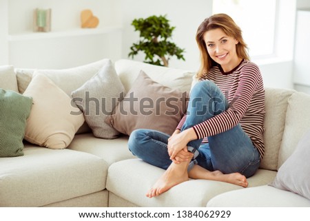 Full length side profile body size photo beautiful she her lady calm hold hands arms pretty long legs wear casual jeans denim striped pullover clothes sit comfort cozy divan house living room indoors