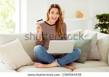 Portrait of her she nice-looking attractive lovely cheerful cheery glad wavy-haired girl sitting on divan lotus position showing new card sale discount in light white interior room
