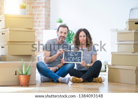 Middle age senior couple sitting on the floor holding blackboard moving to a new home with a confident expression on smart face thinking serious