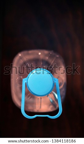 Plastic water bottle in warm light on dark background, selective close view from the top, vertical frame and copy space.