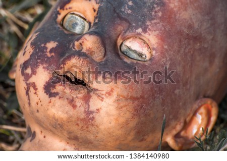 Creepy old doll head. Broken abandoned damaged scary toy in a garbage dump close-up. In the toy, the eye and mouth are damaged. The concept of fear, horror, crime. Very scary