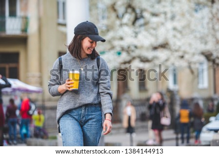 young stylish woman walking by street with coffee cup. spring blooming tree on background