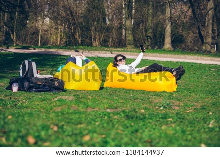 couple laying on yellow inflatable mattress in city park. reading book. taking selfie. leisure time