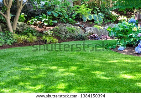 This beautiful backyard woodland garden features a maintenance free lawn made of realistic looking artificial grass, a huge landscaping trend for small spaces. Royalty-Free Stock Photo #1384150394
