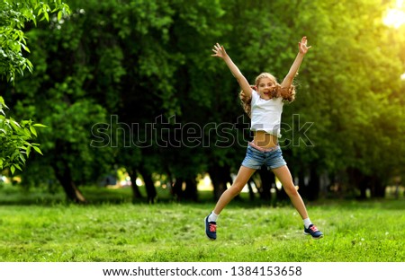 Charming teen girl in shorts and t-shirt jumping and laughing in summer on green background