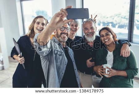 Cheerful multi-ethnic people in the office smiling and taking the selfie. Businessman taking selfie with his colleagues in office.