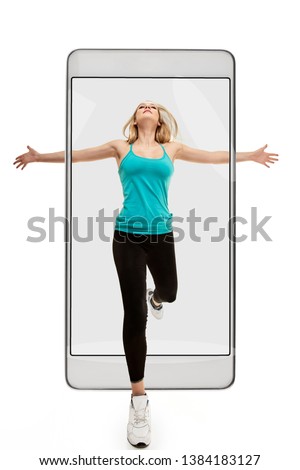 Young athletic happy woman running with raised hands, concept virtual reality of the smartphone. going out of the device