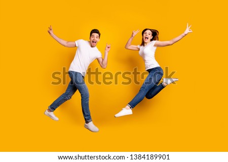 Full length side profile body size photo funky she her he him his pair jumping high yell scream shout fantastic mood show v-sign wear casual jeans denim white t-shirts isolated yellow background