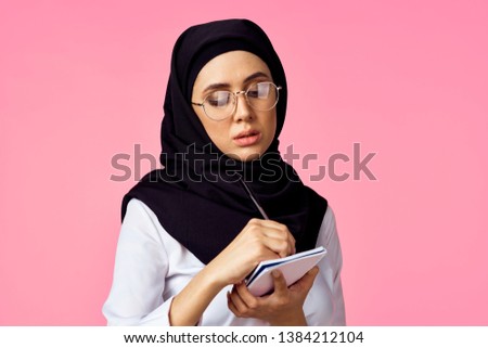 arab woman writing in notebook on a pink background                              